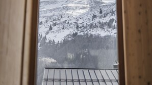 Vista a través de una ventana con marco de madera de un paisaje montañoso nevado.