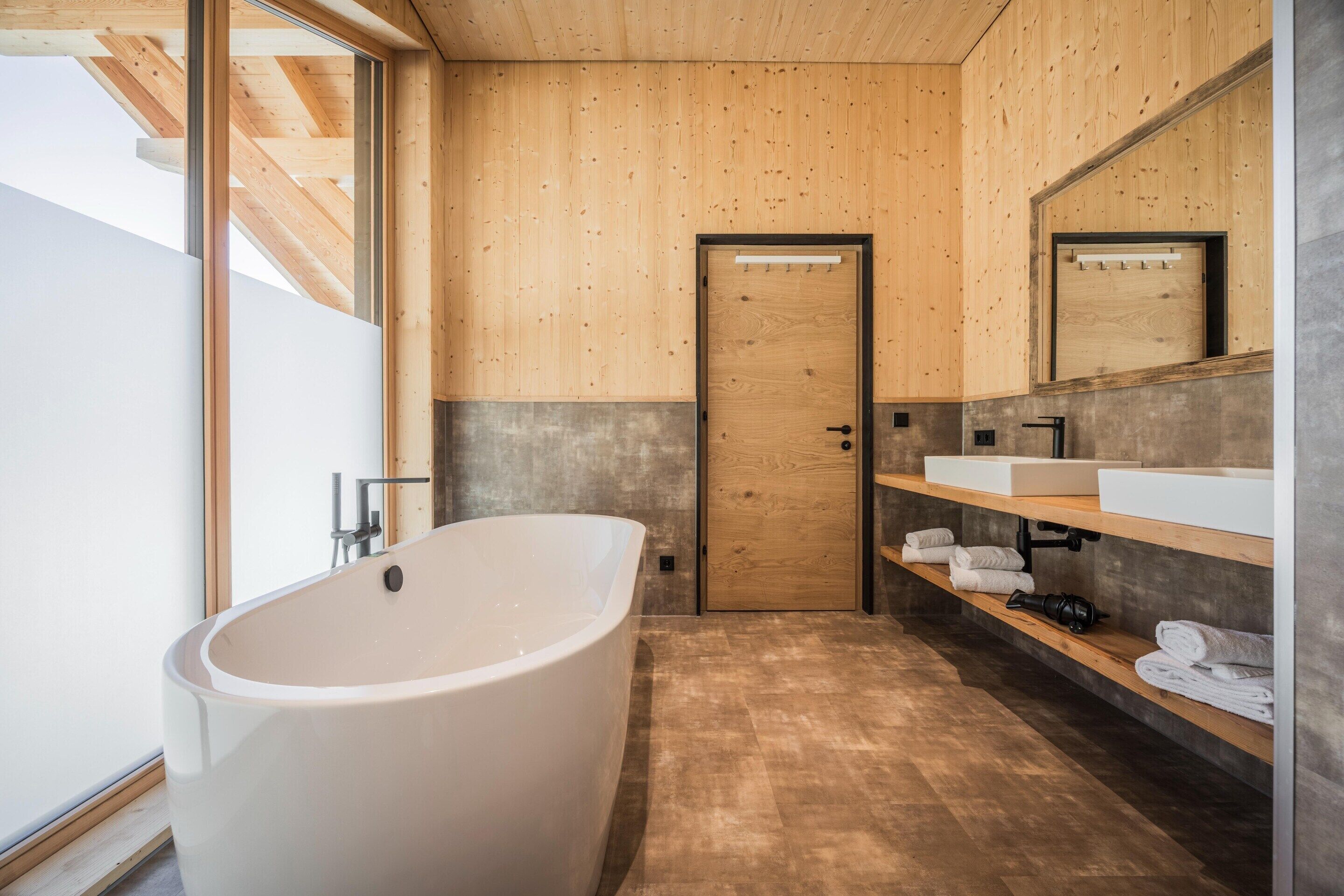 A modern bathroom with a freestanding bathtub, wooden walls, a large mirror, and a wooden shelf with towels.