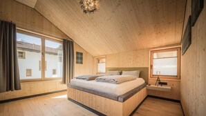 Un dormitorio con techo de madera, una cama grande, una mesita de noche, una ventana con cortinas y vistas a un edificio.