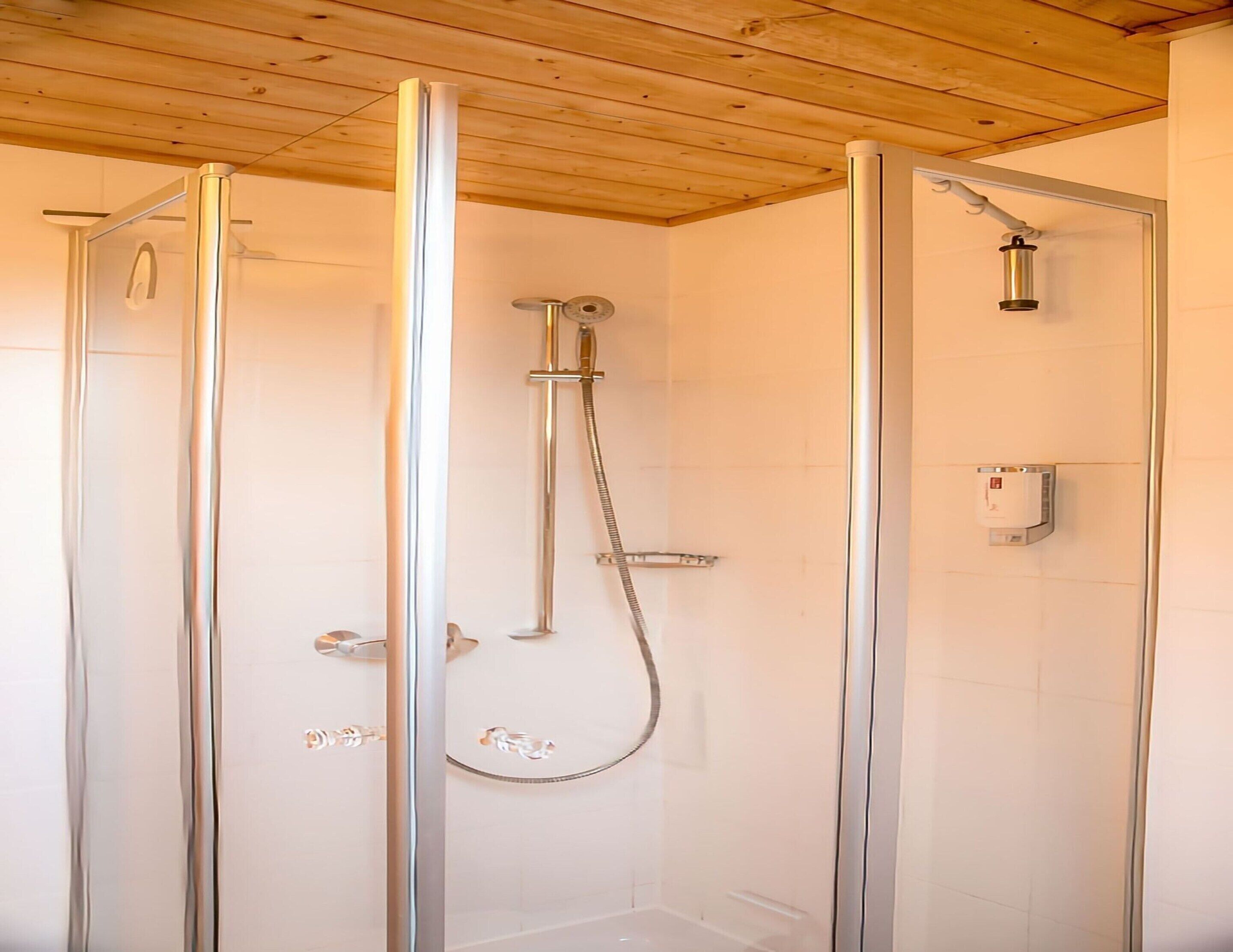 A glass-enclosed shower with a handheld showerhead and a wall-mounted faucet.