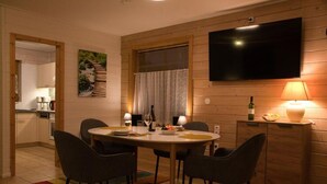 A dining area with a round table, four chairs, a television mounted on the wall, and a cabinet with a lamp. - Doppelhaushalfte in Hasselfelde (Oberharz am Brocken)