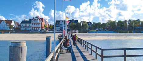 A wooden pier extending into calm waters, with a flagpole and flag in the background.