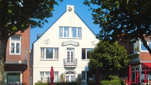 A traditional building with a gabled roof, a balcony with a wrought iron railing, and a sign reading "GUD KOOR". - Studio, Wyk auf Fohr (Wyk auf Foehr)