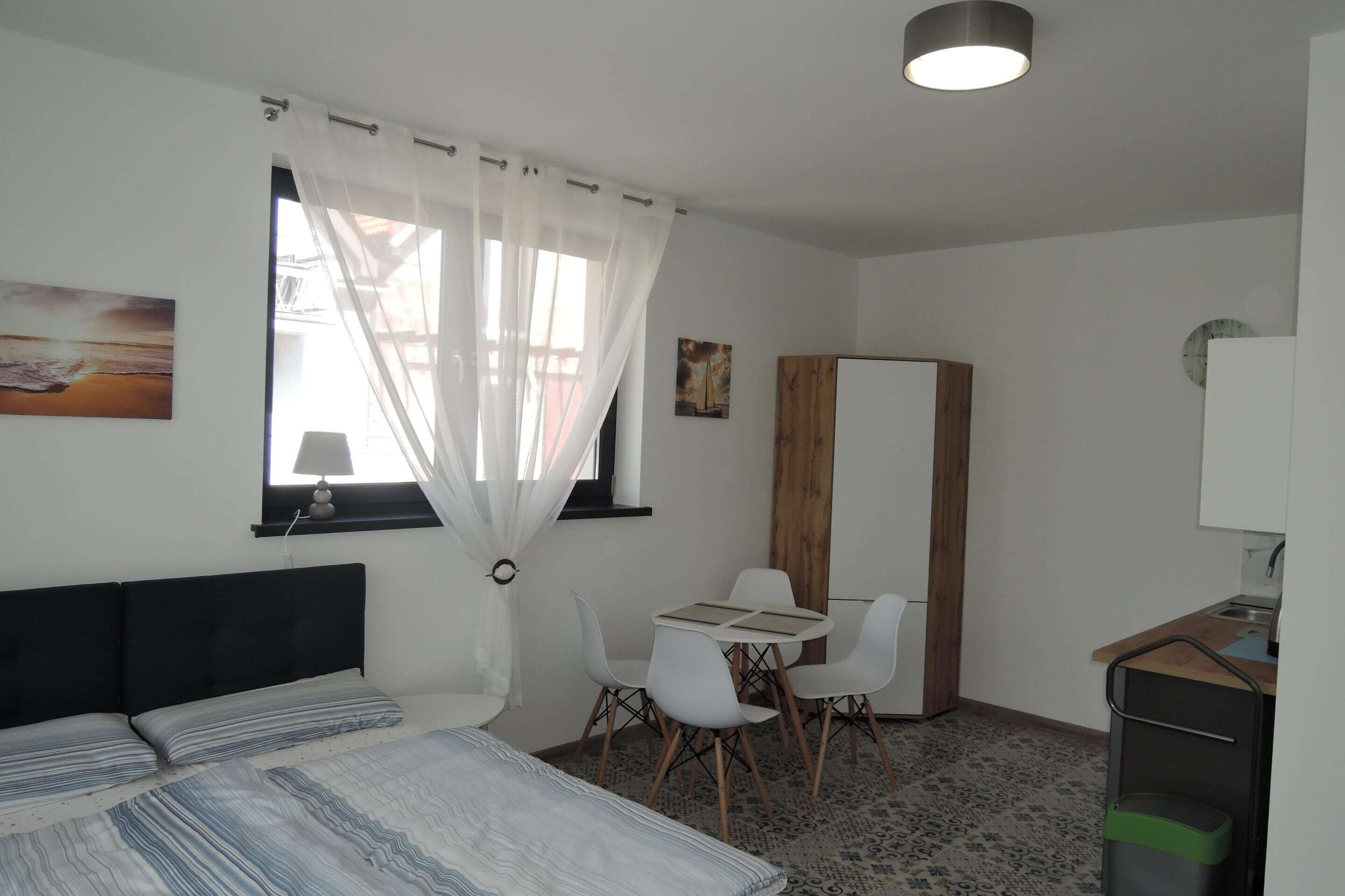 Una camera da letto con un letto, una scrivania, una sedia, una finestra con tende leggere e una sveglia appesa al muro.