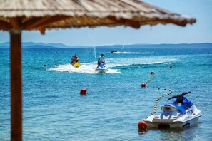 A beach scene with a jet ski, a small boat, and a person on a yellow inflatable. - Apartment on Vir Island Near Sandy Beaches (Vir)