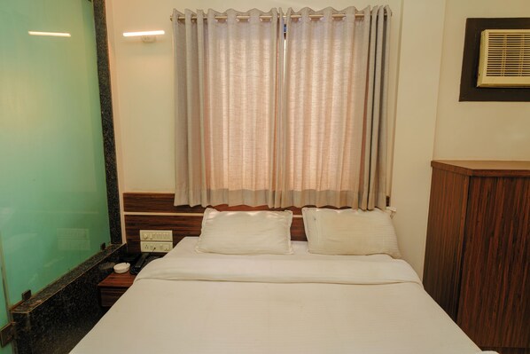 A hotel room with a bed, two pillows, a nightstand, a telephone, and a window with curtains. - Hotel Vinayak Residency (Navi Mumbai)