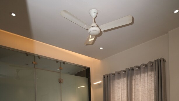 Une chambre à coucher comprenant un lit, un ventilateur de plafond, une armoire et une fenêtre avec des rideaux.