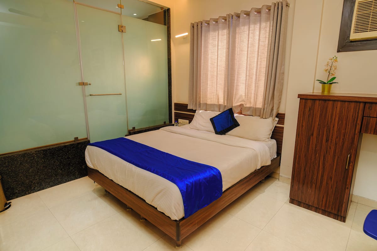 A bedroom with a bed, a wooden cabinet, a mirror, and a window with curtains.