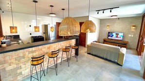 A modern kitchen with a central island, bar stools, and hanging rattan lights.
