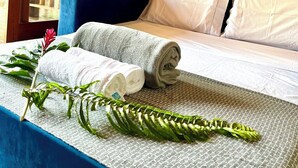 A neatly made bed with white and grey linens, a blue headboard, and a decorative wall hanging.