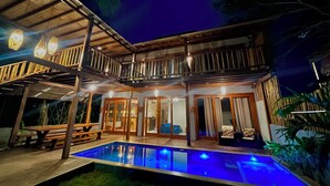 A two-story building with a pool, wooden deck, and outdoor seating.