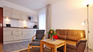A modern living room with a sofa, armchair, coffee table, and a small kitchen area with a microwave. - Appartement in Westerland auf Sylt (Sylt)