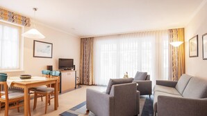A modern living room with a sofa, two armchairs, a dining table with chairs, a TV, and a cabinet. - Ferienwohnung im Dunenpark Binz (Binz)