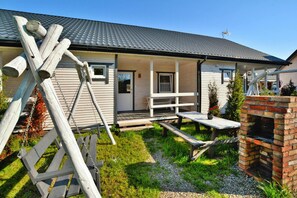 Ein Haus mit Veranda, Schaukel und Kamin aus Backsteinen, sowie ein kleiner Garten.