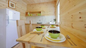 Cocina con paneles de madera, un refrigerador blanco, una mesa de madera dispuesta con cuencos y platos verdes, y una ventana que deja entrar luz natural.