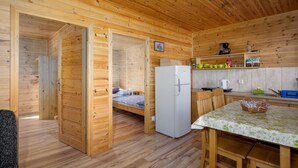 Interior de una cabaña de madera con cocina, comedor y un dormitorio con cama y cómoda.