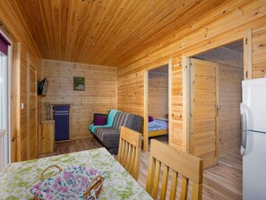 Ein gemütliches Blockhaus-Interieur mit Holzbalkendecke, einer Couch, einem Tisch mit floralem Tischtuch und einem Kühlschrank.