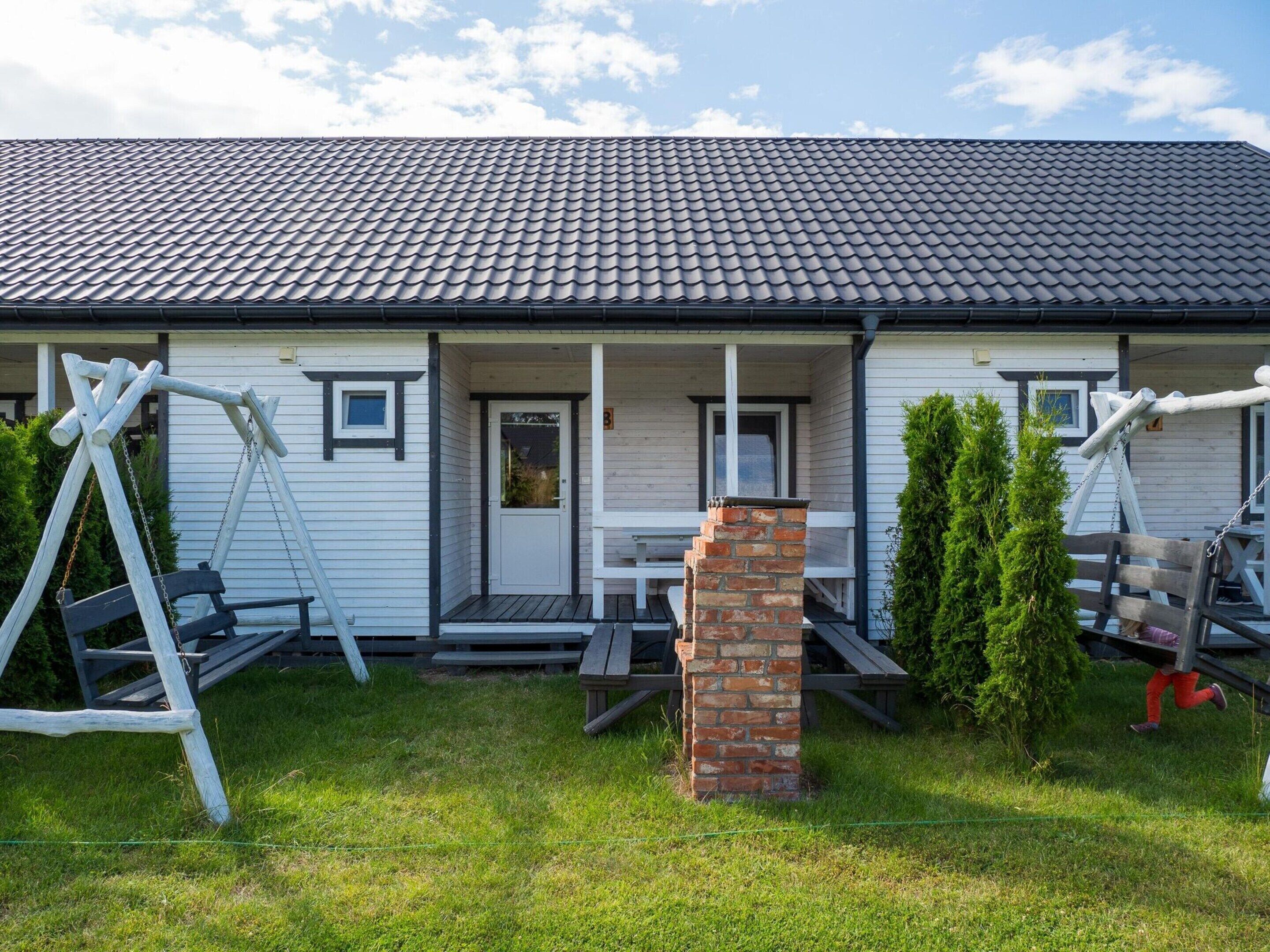 A house with a porch, a brick chimney, and a swing set.