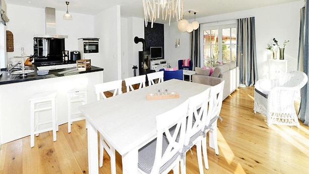 Una cocina moderna con una isla central, zona de comedor blanca y un rincón de estar acogedor con sofá y sillas.