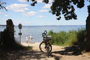 A bicycle parked on a sandy path by a lake with a signpost and two people in the background. - Gemutliche Ferienwohnung in Mallentin (Stepenitztal)