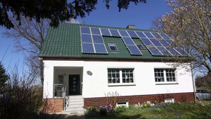 Una casa con paneles solares en el techo, cimientos de ladrillo y un jardín con flores.