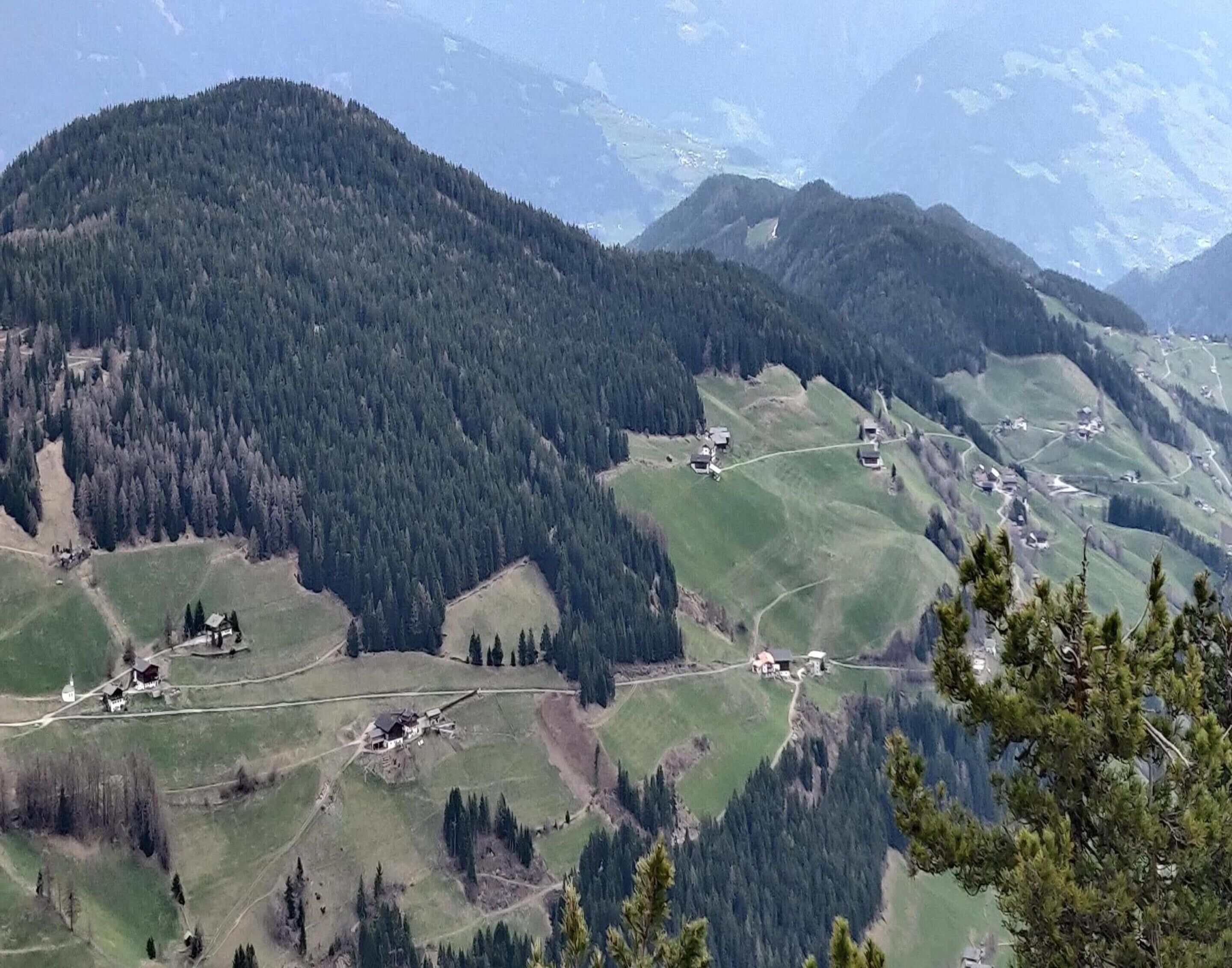 A mountainous landscape with scattered buildings, likely a rural area with houses and possibly a small church.