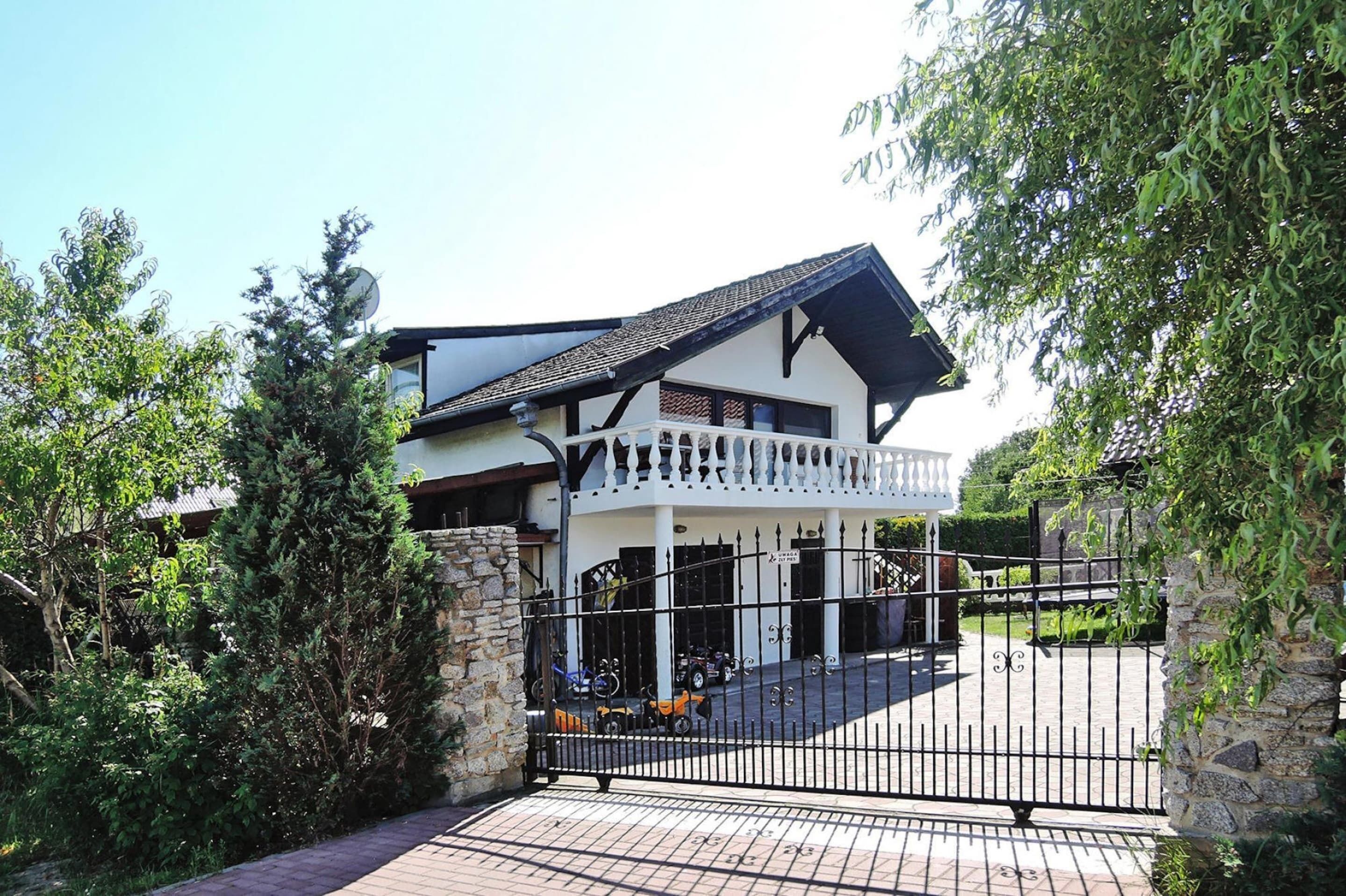 A two-story house with a balcony, a gated driveway, and a stone wall.
