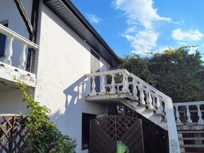 A white building with a balcony, a wooden gate, and a tree in the background. - Holiday Home in Stepnica (Stepnica)