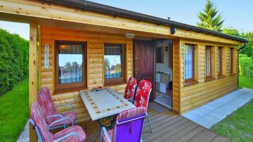 A wooden cabin with a deck, a dining table, and four chairs.