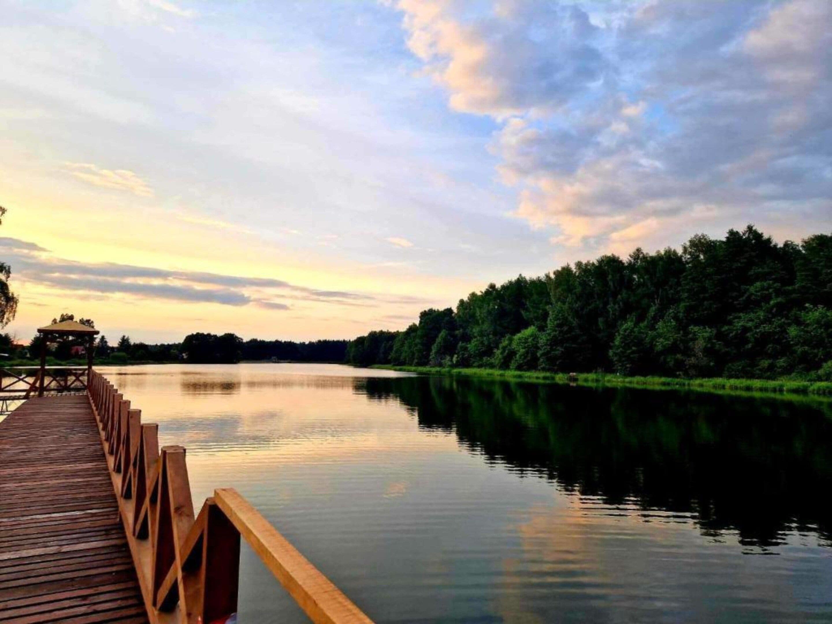 A wooden pier extending into a calm lake with a forested shoreline.