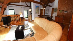 A spacious living room with a large beige sofa, wooden beams, a television on a stand, and a dining area with chairs and a table. - Ferienhaus, Zahrensdorf (Kloster Tempzin)