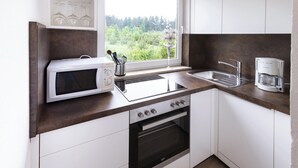 A compact kitchen with white cabinets, a built-in microwave, a stove, a coffee maker, and a window with a view of greenery. - Adults Only Apartment With Pool (Sankt Kanzian am Klopeiner See)
