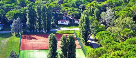 Zona residencial con casas rodeadas de abundante vegetación, una cancha de tenis y un césped cuidado.