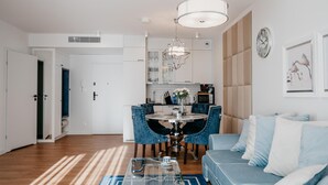 Een moderne woonkamer met een bank, een salontafel en een eetgedeelte met stoelen en een kroonluchter.