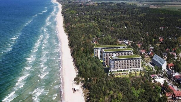 Luchtbeeld van een kustgebied met een strand en een hotelcomplex met een groen dak.