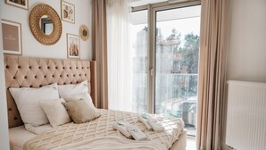 Een slaapkamer met een gestoffeerd hoofdeinde, een groot bed met meerdere kussens, uitzicht op een stadsbeeld door een schuifdeur en een witte radiator.