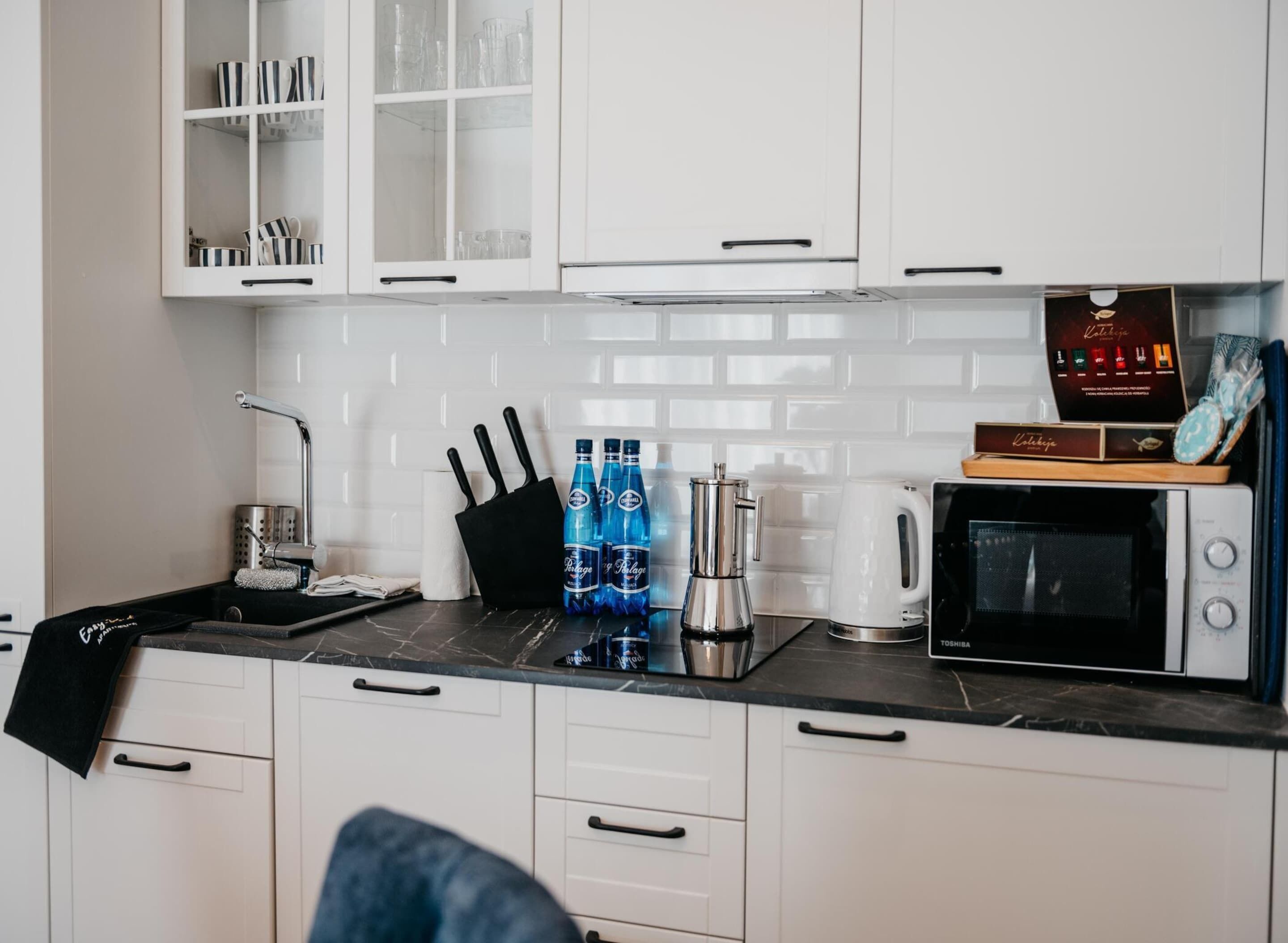 A modern kitchen with white cabinets, a black countertop, a coffee machine, and a microwave.