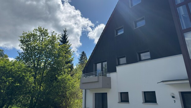 Ein modernes Gebäude mit zahlreichen Fenstern und Balkonen, umgeben von üppigem Grün.