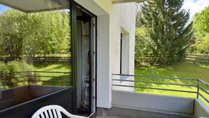 Ein Balkon mit Tisch und Stuhl, einer Glastür und Blick auf eine grüne Landschaft mit Bäumen.