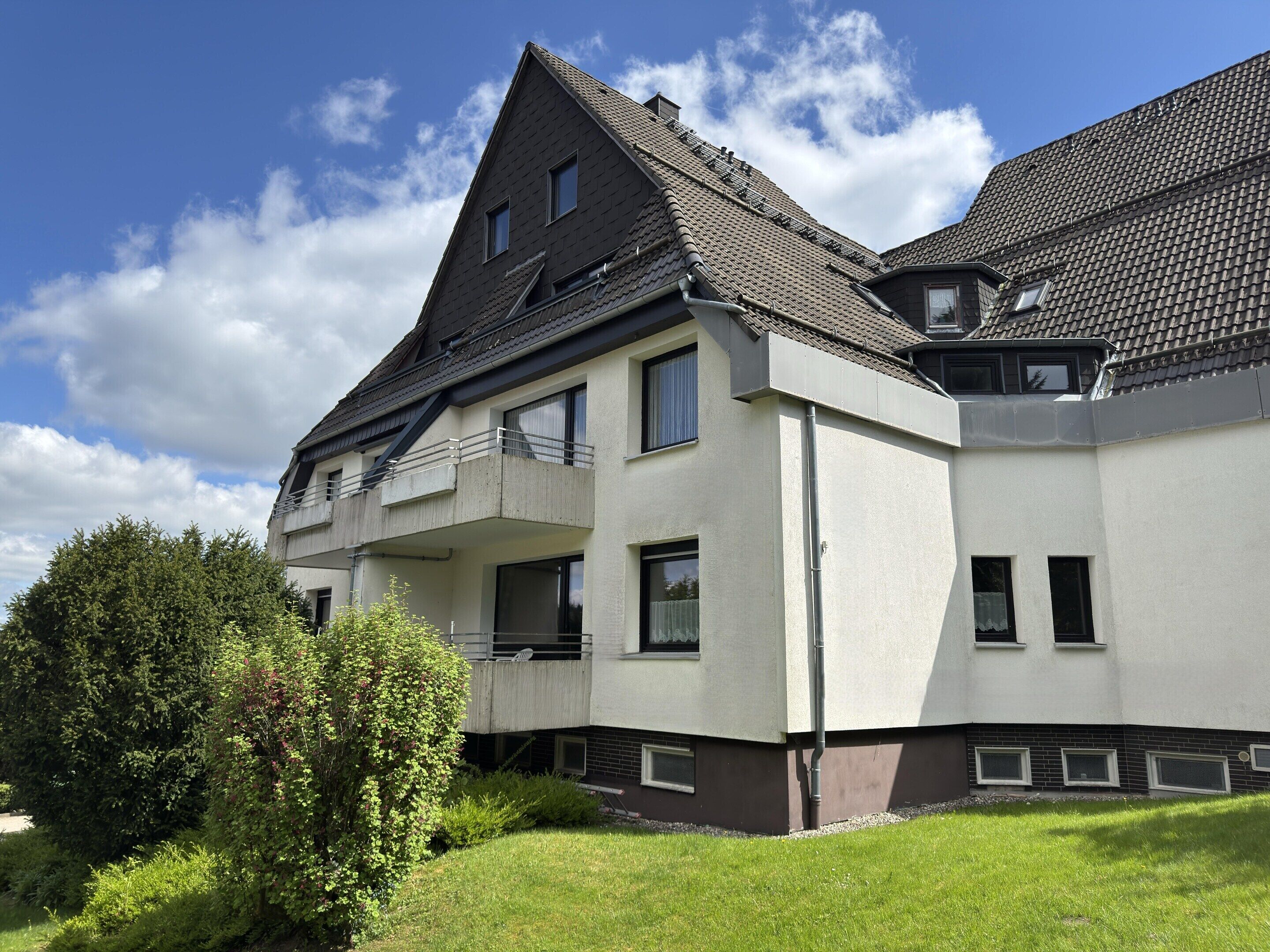 Ein mehrstöckiges Gebäude mit geneigtem Dach, Balkonen und einem gepflegten Rasen.