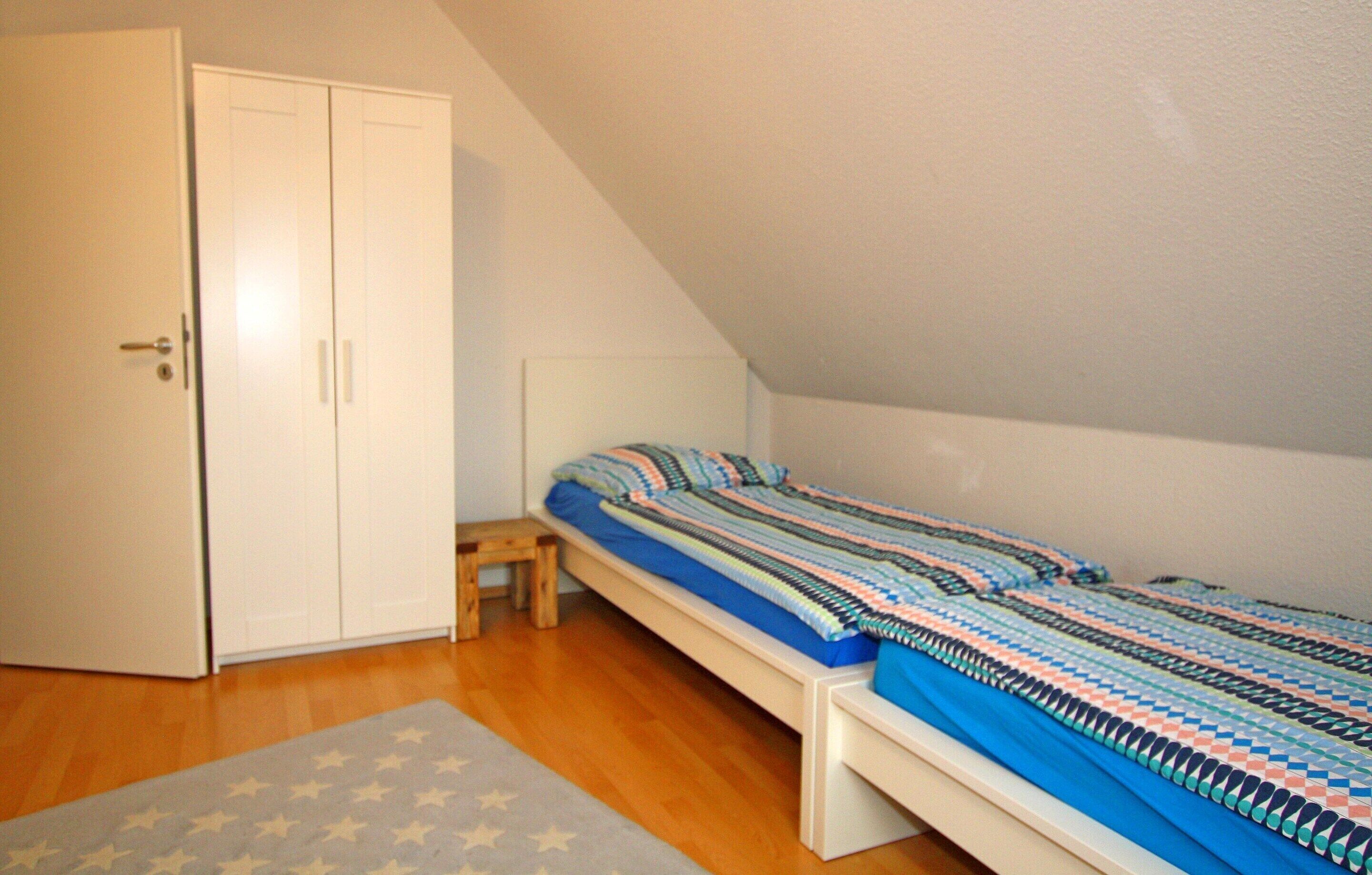 A bedroom with a single bed, a wardrobe, and a small wooden stool.