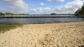 A sandy beach with a water body, a white bridge, and a playground structure. - Ferienhaus Barbara, Zarrentin (Zarrentin am Schaalsee)