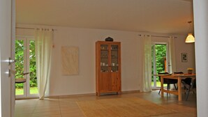 A spacious room with a wooden cabinet, a dining table, and a large window with curtains. - Ferienhaus Barbara, Zarrentin (Zarrentin am Schaalsee)