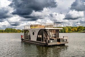 A floating houseboat with a deck, windows, and a staircase leading to an upper level.