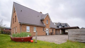 A two-story brick house with a sloped roof, a gravel driveway, and a wooden fence. - Doppelhaushalfte in St. Peter-ording (St. Peter-Ording)