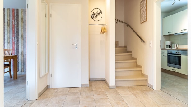 A modern kitchen with stainless steel appliances, a dining area with a wooden table and chairs, and a staircase leading to an upper floor. - Doppelhaushalfte in St. Peter-ording (St. Peter-Ording)