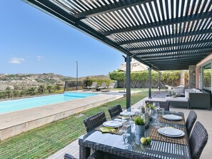 Un espacio al aire libre cubierto con piscina, mesa de comedor preparada para cuatro personas y sillones de descanso.