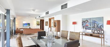 A modern dining area with a glass-top table, wicker chairs, and a sofa in the background.