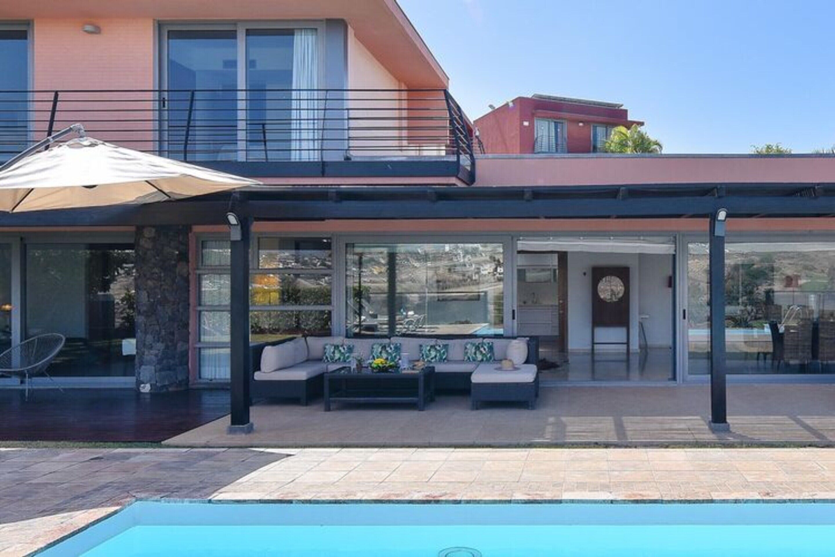 A modern house with a covered patio, a pool, and a balcony.