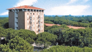 A multi-story building with balconies, surrounded by dense greenery and a clear sky.